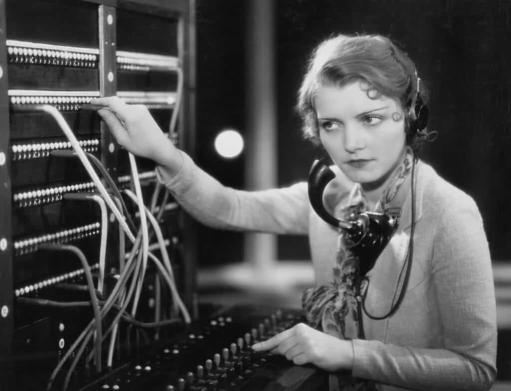 Woman operating a vintage telephone switchboard, illustrating early human intermediaries in communication, reflecting the evolution of search technology from town operators to AI agents.